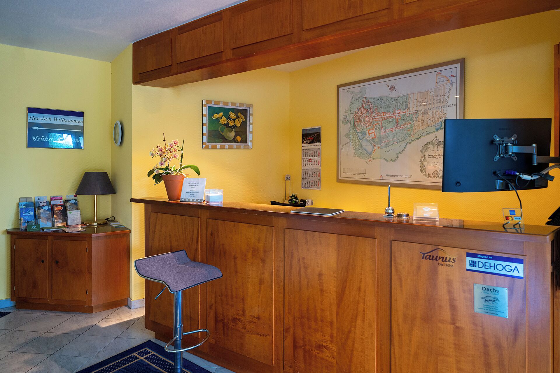 A reception desk with a wooden finish, a map on the wall, a potted plant, and a bar stool.