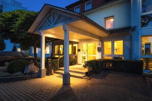 Ein Hotel mit Eingangsbereich, überdachter Veranda und einem parkenden Auto vor einer gut beleuchteten Fassade.
