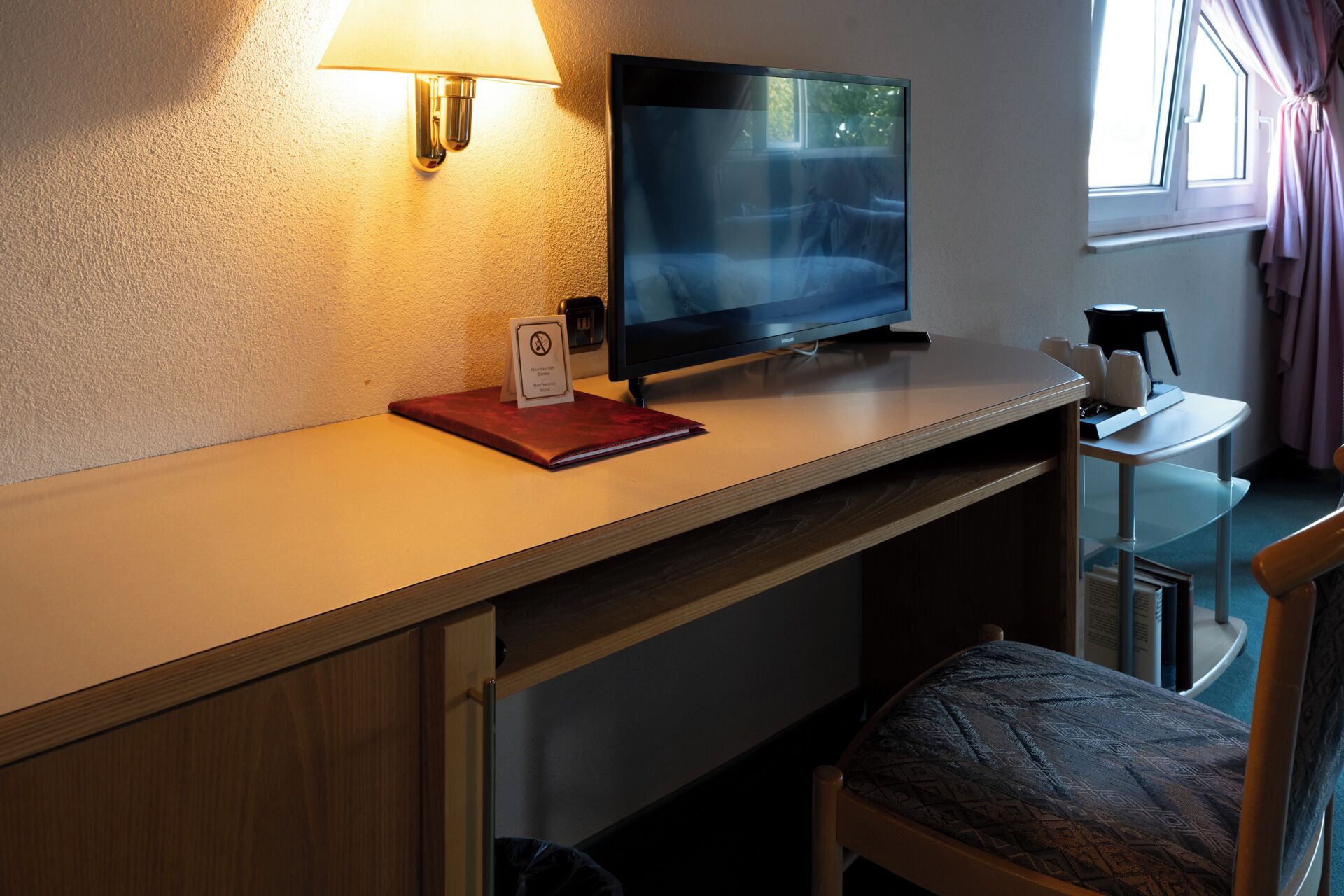 A hotel room with a bed, a desk with a lamp, a television, and a coffee machine.