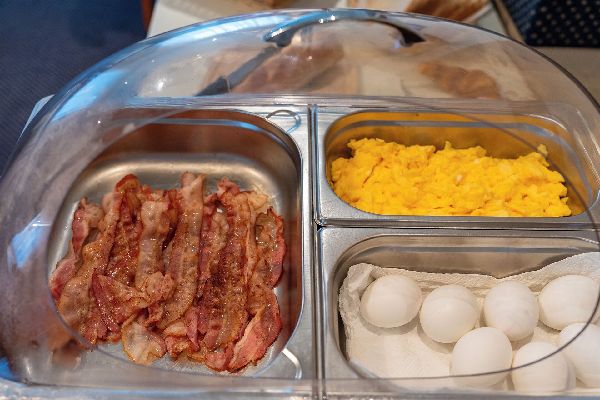 Ein Frühstücksbuffet mit drei Bereichen: Speck, Rührei und gekochte Eier.