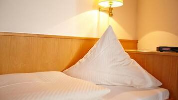 A neatly made bed with white linens and pillows, a bedside table with a lamp, and a digital clock.