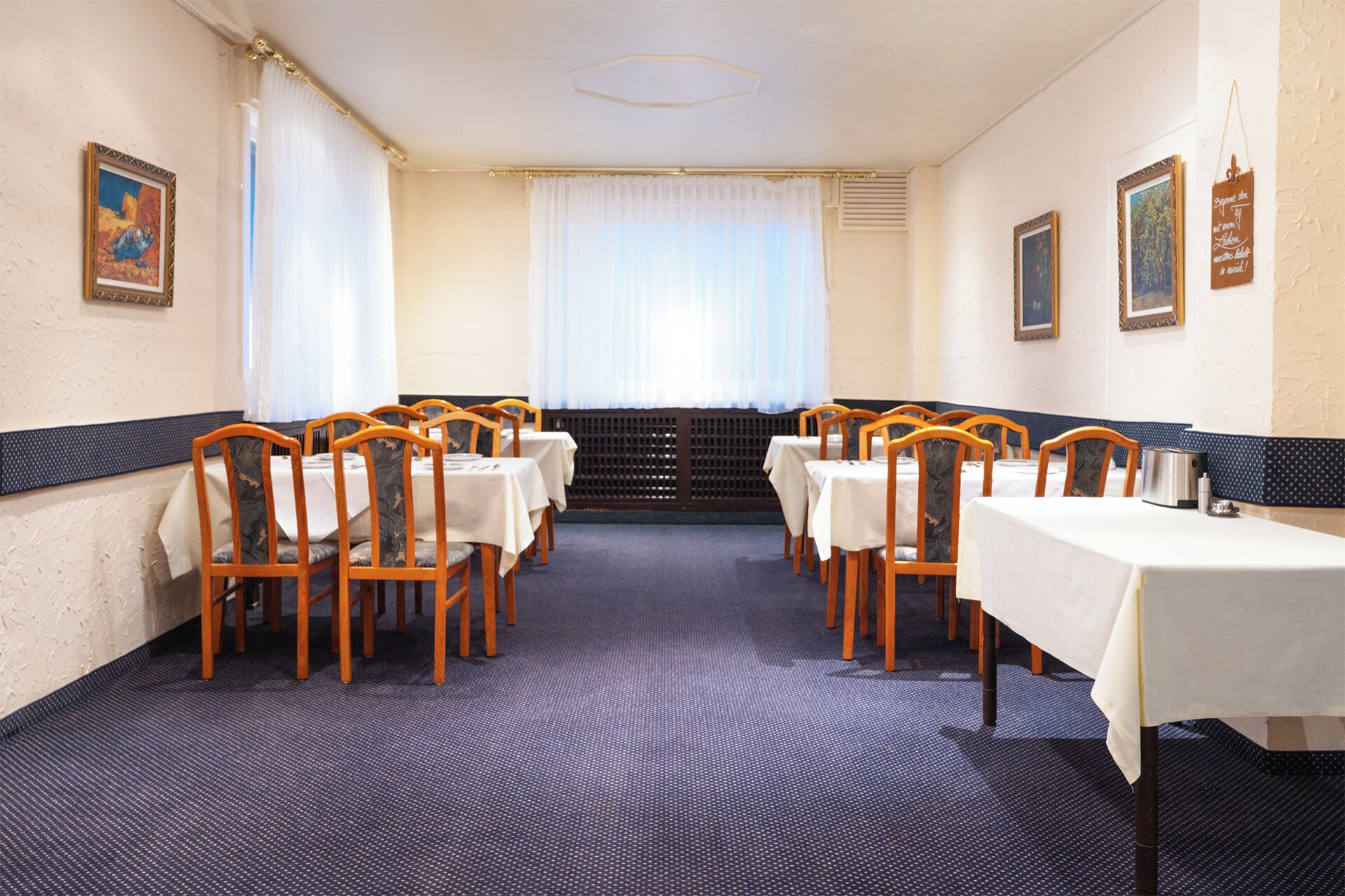 Un salón de conferencias con mesas y sillas, un ventanal con cortinas y cuadros en las paredes.