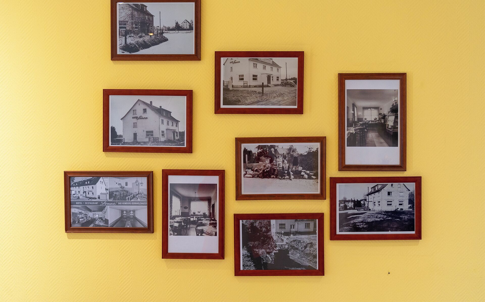 A collection of black and white photographs of buildings and interiors, likely historical, displayed on a yellow wall.