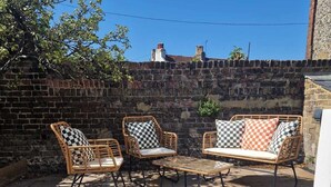 Un espace extérieur aménagé en terrasse, avec un sol en pierre, des meubles en osier et un mur en briques.
