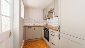 Une cuisine compacte avec des meubles blancs, un plan de travail en bois et un pare-feu en carreaux.