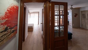A hallway with a wooden door, a painting on the wall, and a view into a room with a bed.
