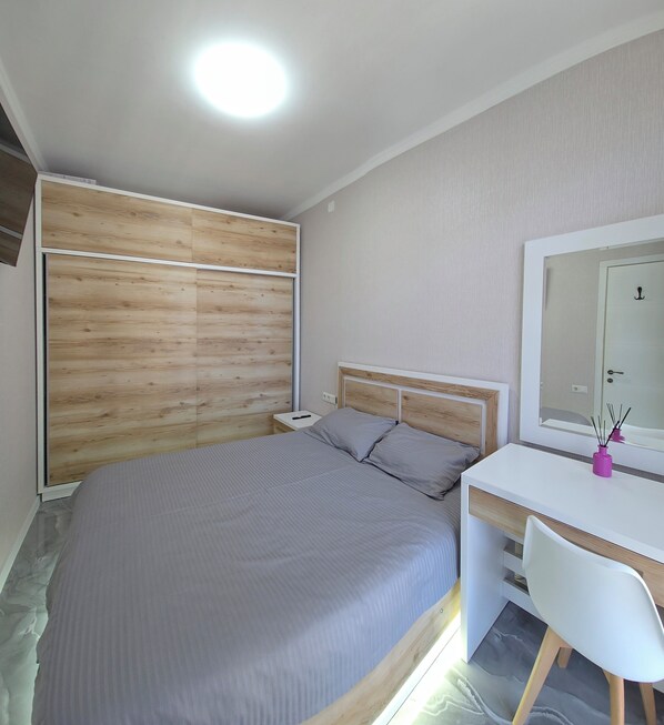 A bedroom with a bed, bedside table, and a desk with a chair.