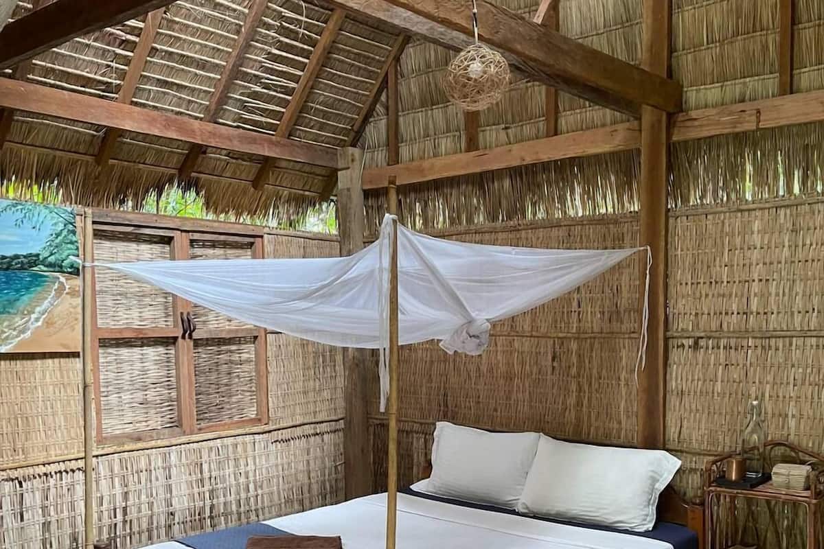 A wooden bed with a canopy, a woven wall, and a thatched roof.