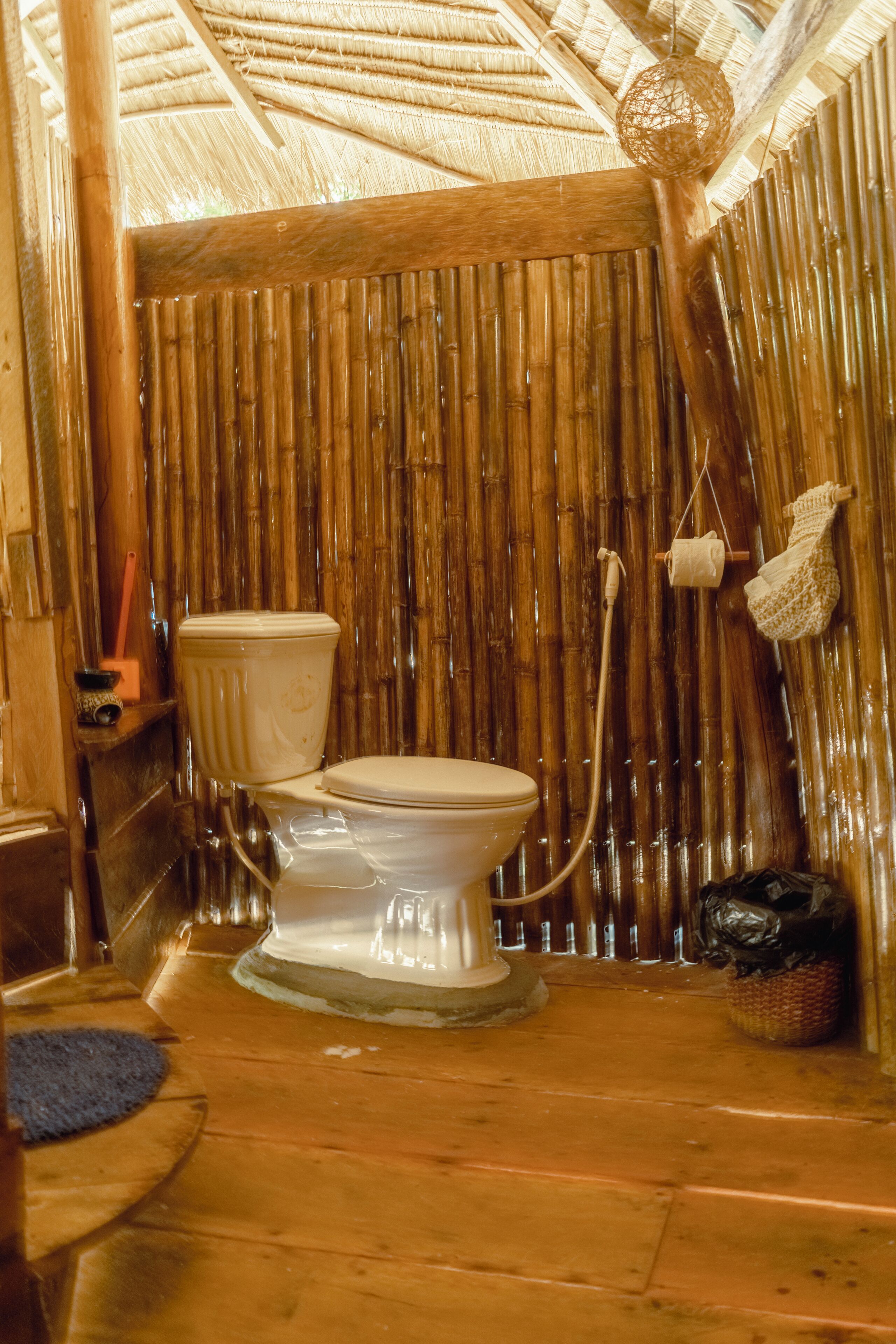 A bamboo-walled bathroom with a toilet, a shower, and a hanging light fixture.