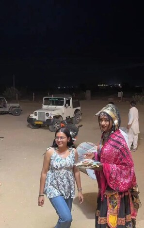 Two people outdoors at night with a vehicle in the background. - Hotel Robin Jaisalmer (Jaisalmer)
