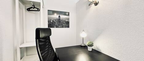 A modern dining area with a black table, a white chair, a wall-mounted lamp, a small potted plant, and a cityscape picture on the wall.
