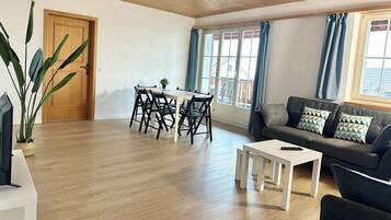 Un vaste espace de vie doté d’un plafond en bois, d’une table à manger avec des chaises, d’un canapé avec des coussins et d’un téléviseur posé sur un meuble.