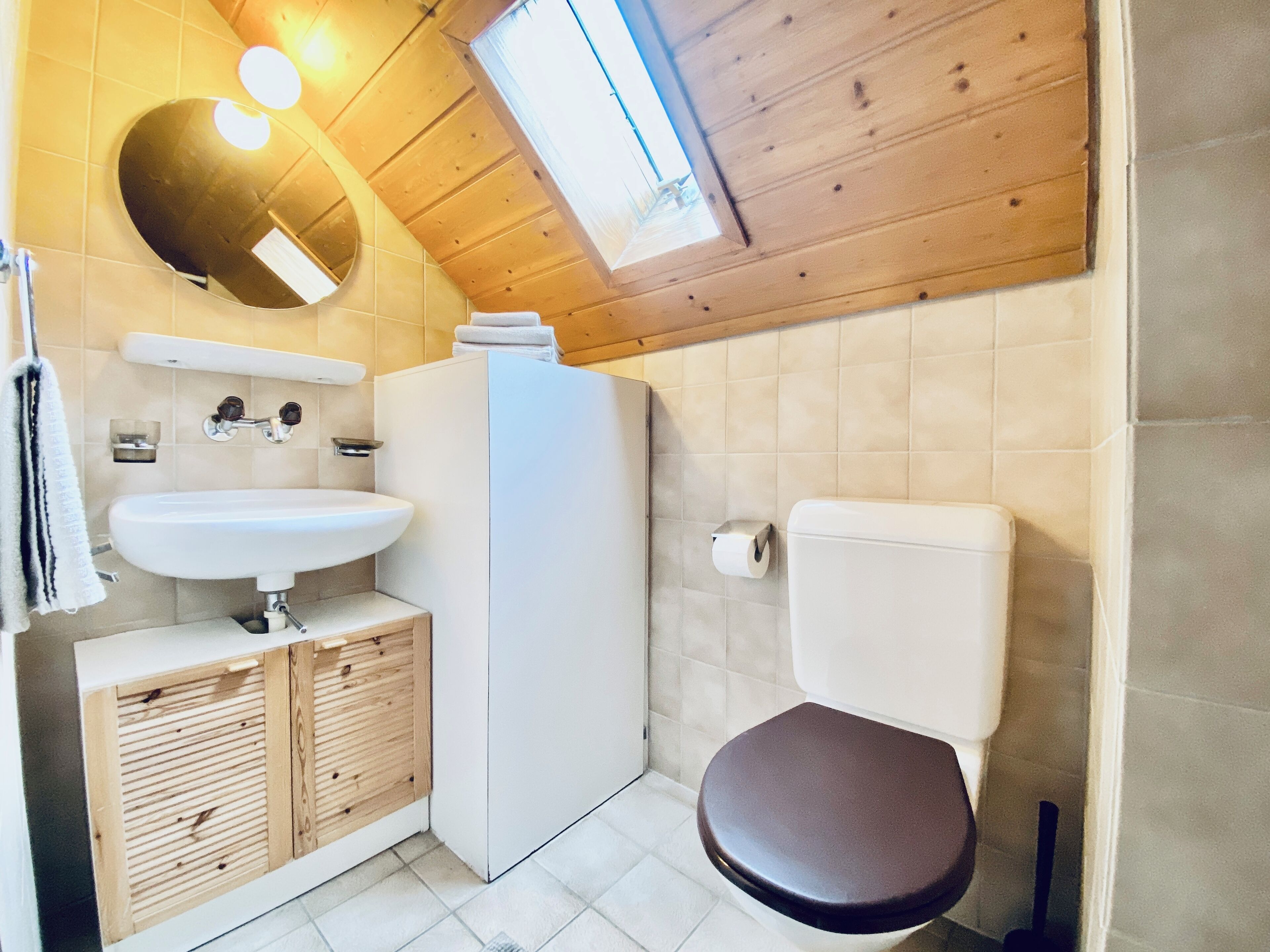 Une salle de bain avec un plafond en bois, un lavabo blanc, des toilettes et un miroir.