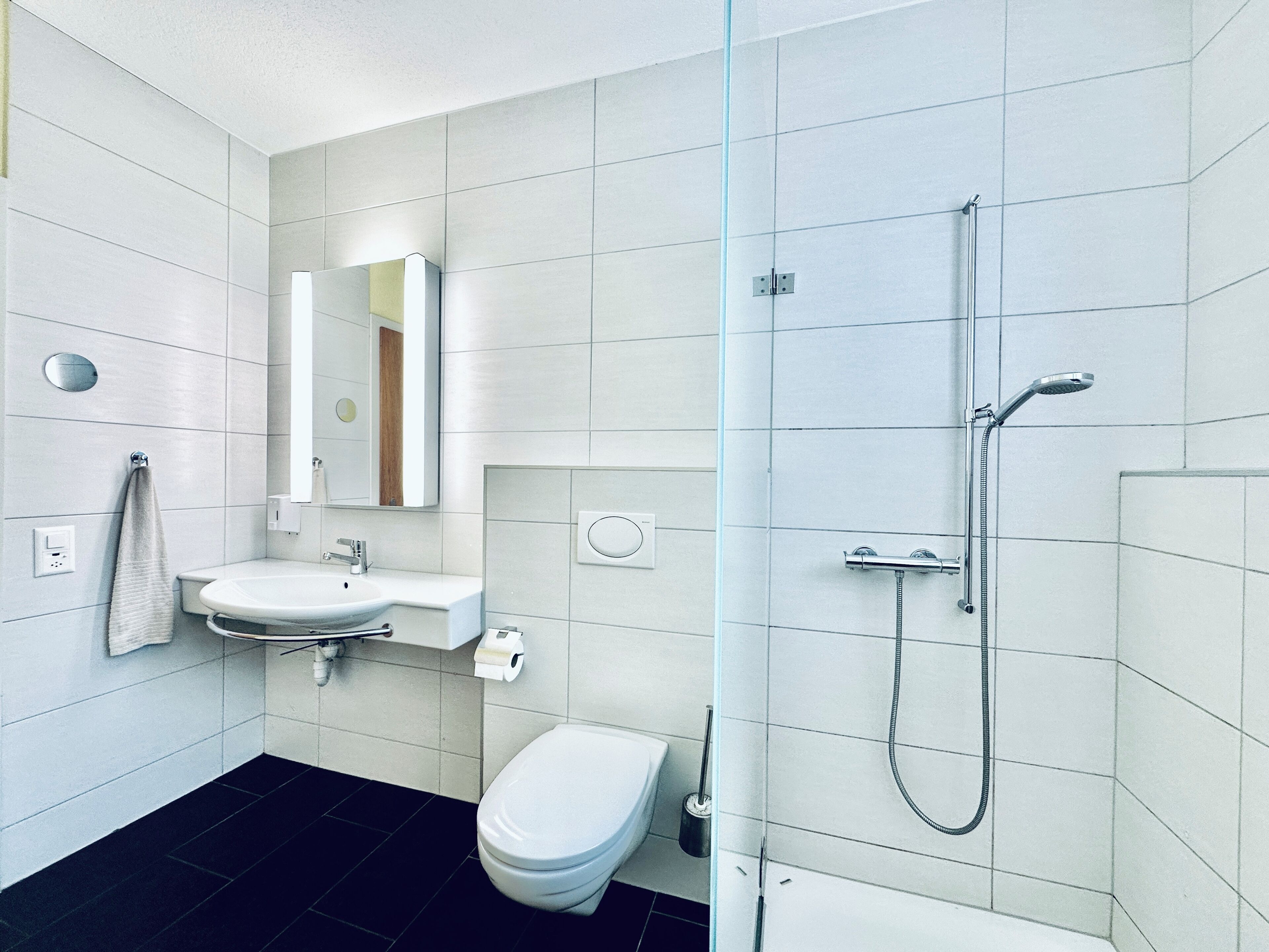 A modern bathroom with a white sink, mirror, toilet, and shower.