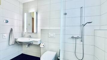 A modern bathroom with a white sink, mirror, toilet, and shower.