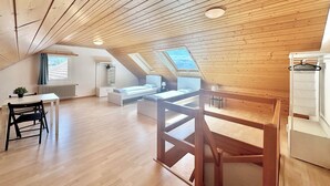 Ruime slaapkamer op zolder met houten balken, een dakraam, een bed, een bureau en een stoel.