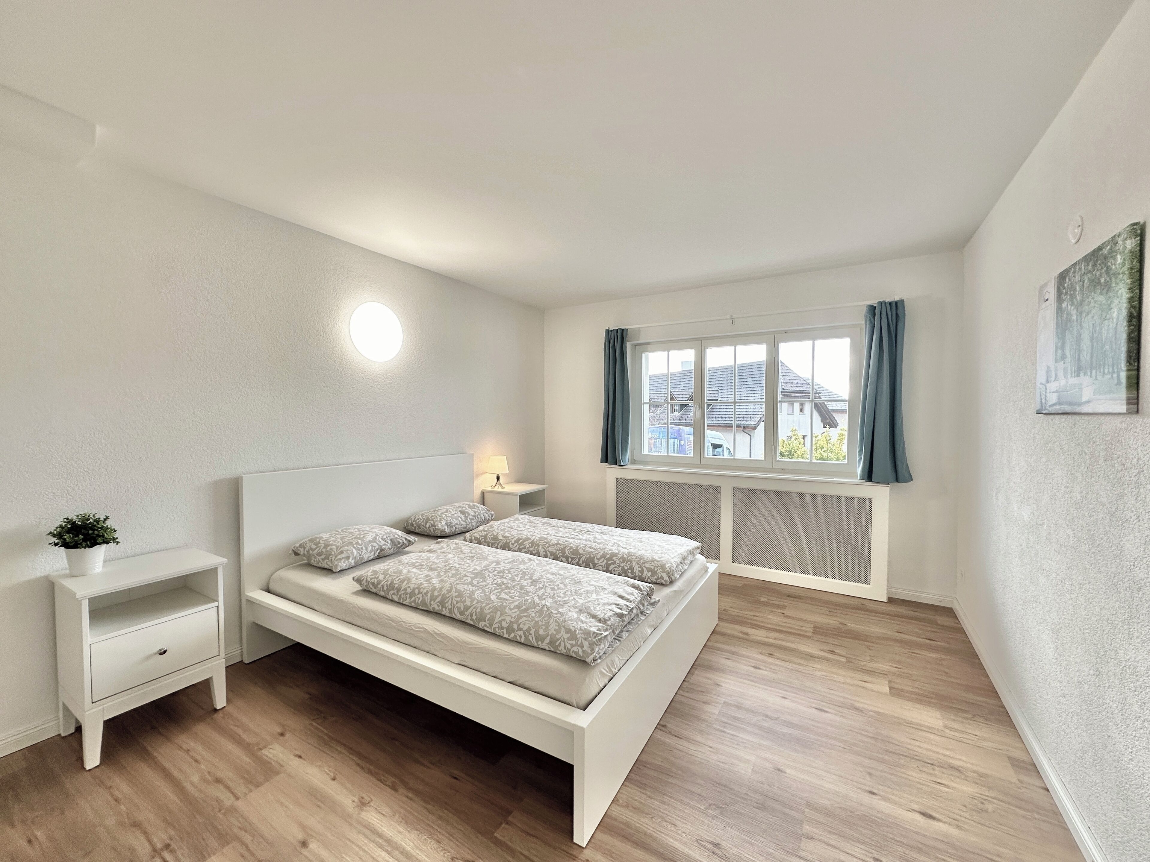 A modern bedroom with a large bed, bedside tables, a potted plant, and a window with curtains.