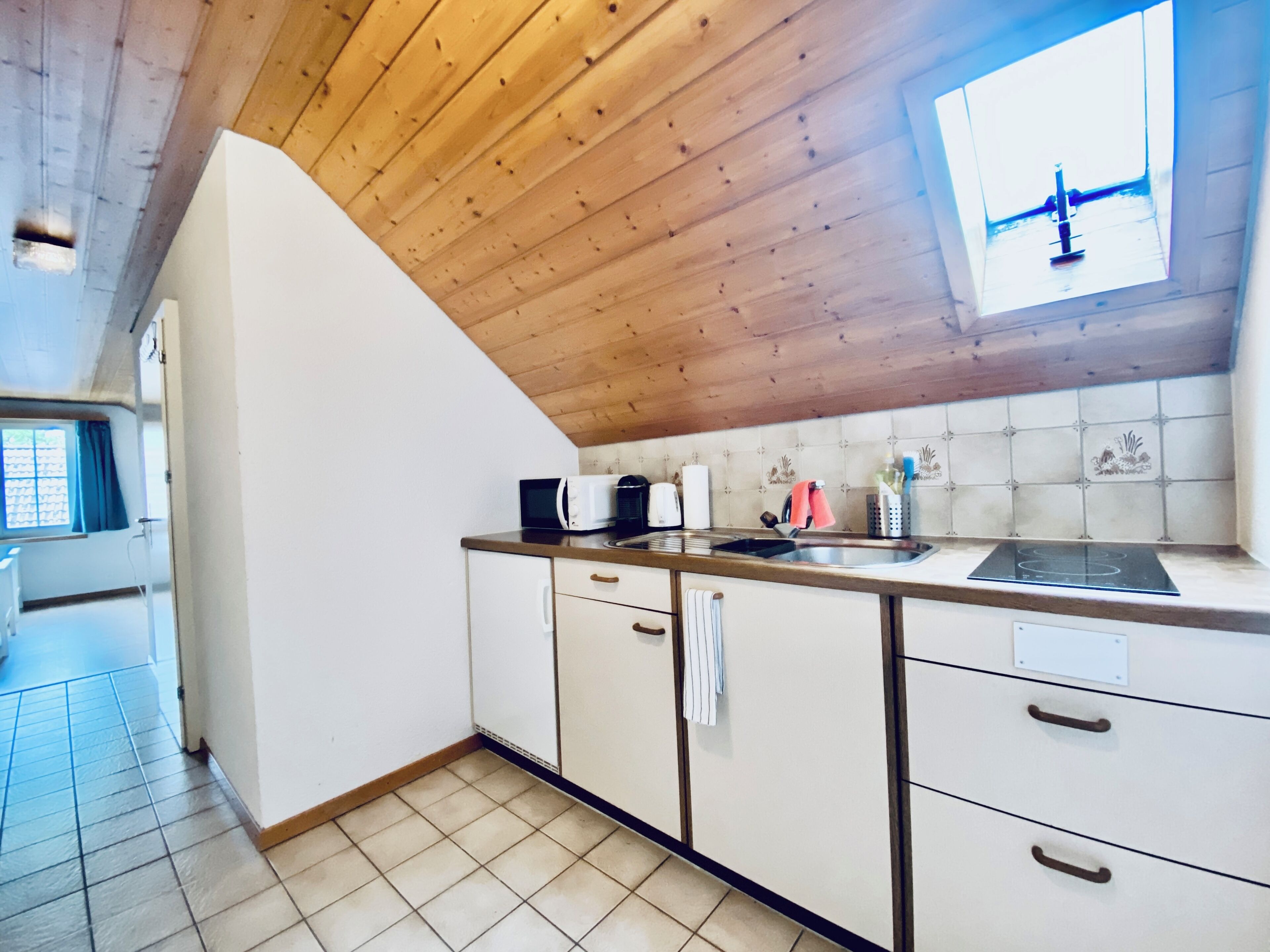 Een keuken met houten plafond, witte kasten, een spoelbak en een raam met uitzicht.