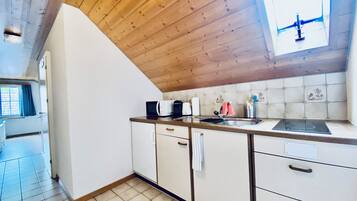 Een keuken met houten plafond, witte kasten, een spoelbak en een raam met uitzicht.