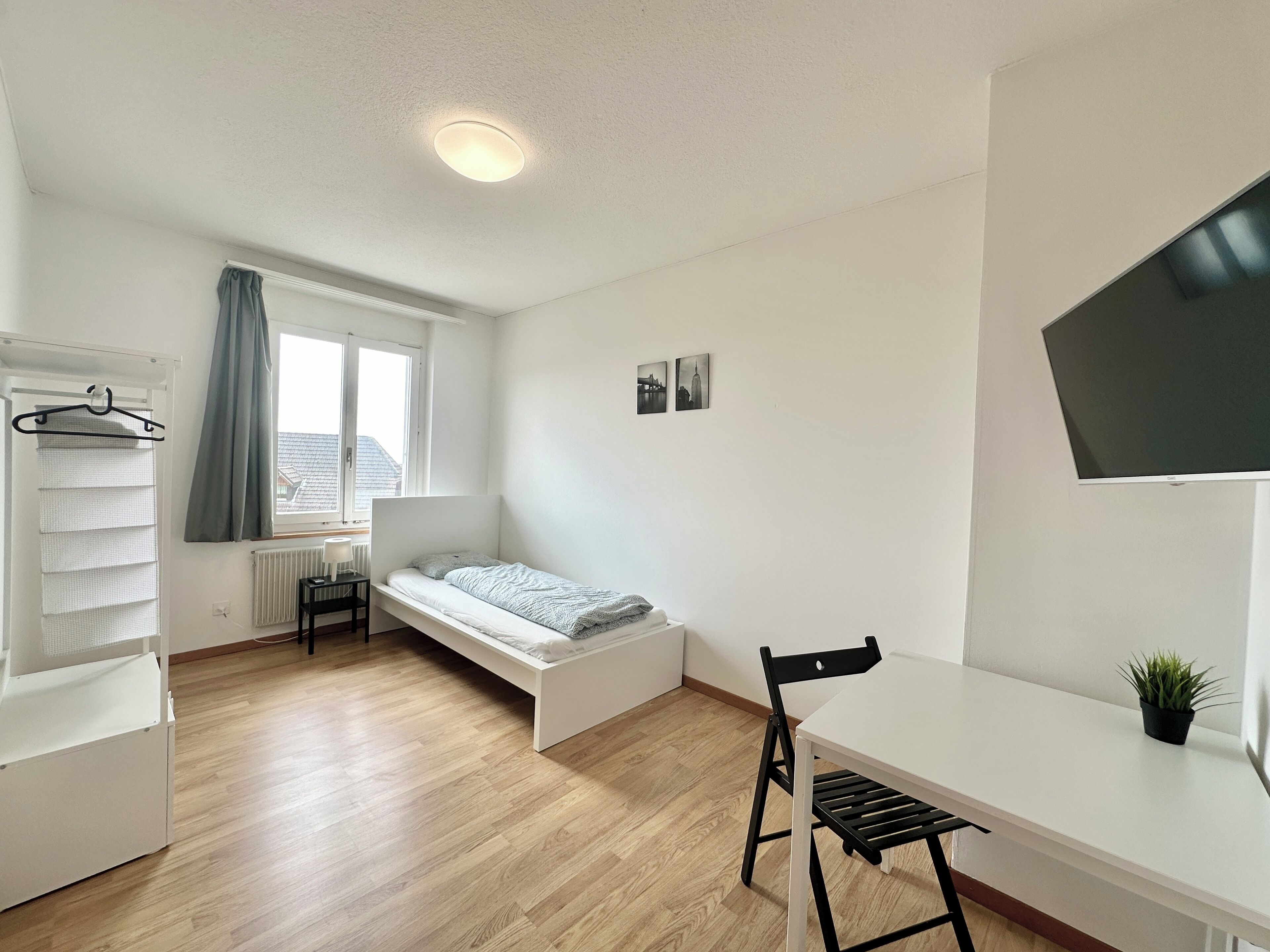 Une petite pièce lumineuse, équipée d’un lit, d’un bureau, d’une chaise et d’un téléviseur.