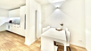 Een moderne keuken met witte kastjes, een ingebouwde oven en een eethoek met een witte tafel en stoelen.