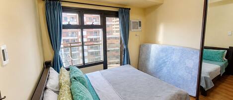 Un dormitorio con cama, mesita de noche, espejo y ventana con cortinas.