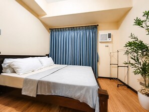 A hotel room with a bed, a window with blue curtains, an air conditioning unit, and a potted plant. - Luxurious Haven in the Sky (Pasay)