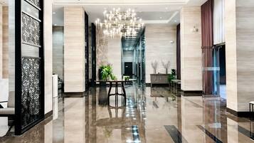 A spacious lobby with a reflective floor, a central chandelier, and a seating area with tables and chairs.