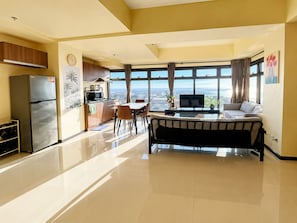 A modern kitchen with a refrigerator, stove, and microwave. There is a dining area with a table and chairs, and a sofa. The room has large windows with a view of the city. - Luxurious Haven in the Sky (Pasay)