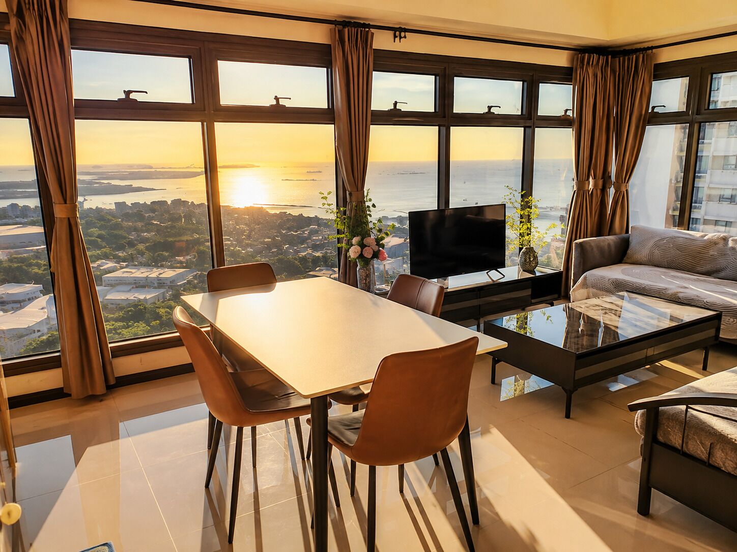 Una sala moderna con comedor, ventanas grandes con cortinas, un televisor de pantalla plana y un sofá.