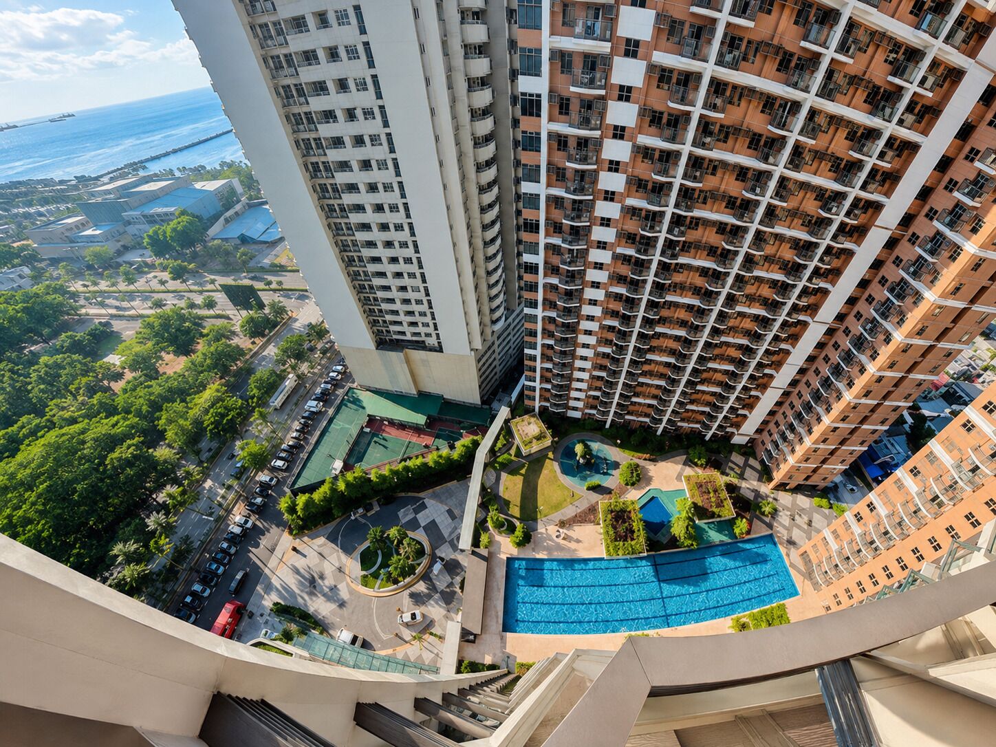 Un edificio residencial de gran altura con varios balcones, una piscina y una zona ajardinada con árboles y un camino de entrada circular.