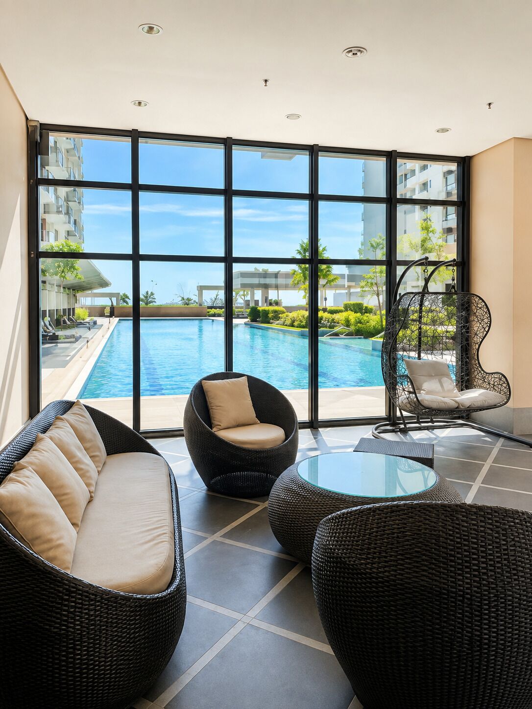 Un espacio lounge moderno con mobiliario de mimbre, una mesa de vidrio y vista a una piscina.