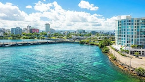 Paisaje urbano frente al agua con edificios modernos, un puente y cielo azul despejado.