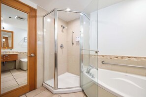 Ein modernes Badezimmer mit einer in Glas abgeschlossenen Dusche, einer Badewanne mit Haltegriff und einer Holztür zu einem Bereich mit Waschtisch.