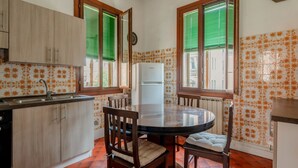 Uma cozinha com mesa, cadeiras, geladeira e janela com persianas.