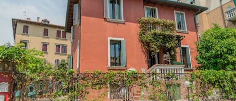 Un edificio rojo con una estatua en la fachada, una cerca cubierta de enredaderas y edificios vecinos.