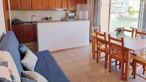 Eine kompakte Küche mit Holzausstattung, ein Essbereich mit Tisch und Stühlen sowie ein Balkon mit Blick auf Gebäude.
