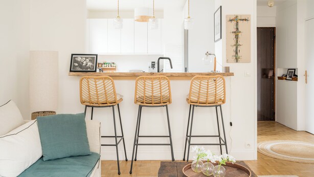 A modern kitchen with white cabinets, a wooden countertop, and three wicker bar stools.