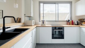 A modern kitchen with a black sink, white cabinets, a window, and a wooden countertop.
