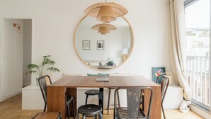 A dining area with a wooden table, four chairs, a hanging light fixture, a mirror, and a potted plant.