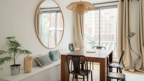A dining area with a wooden table, chairs, a hanging light fixture, a round mirror, and a potted plant.