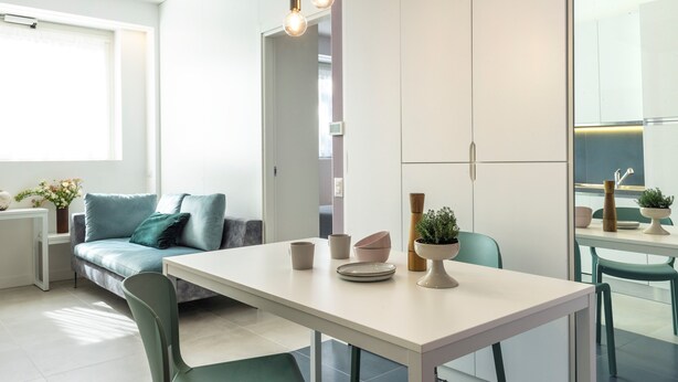 A modern kitchen with white cabinetry, a dining table, and a built-in oven. - 7Studios - 6 Purple (Milano)