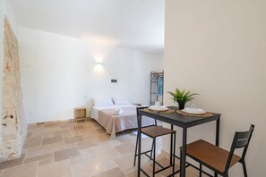 Un dormitorio con cama, mesita de noche y una pequeña mesa con una planta y un vaso.