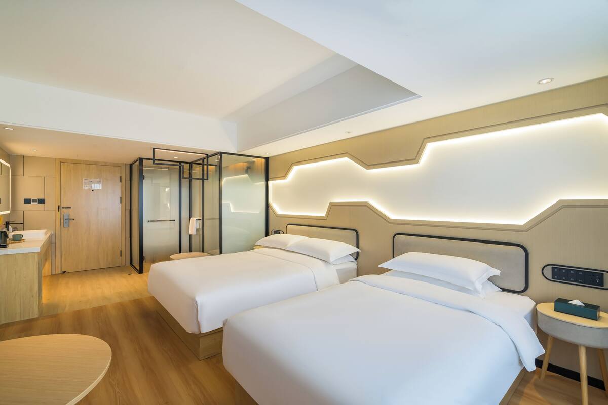 A modern hotel room with two beds, a desk, and a small round table.