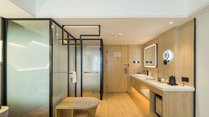 Ein modernes Hotelzimmer mit Bett, einer kleinen Sitzecke, einem Schminktisch mit Spiegel und einer Duschkabine.