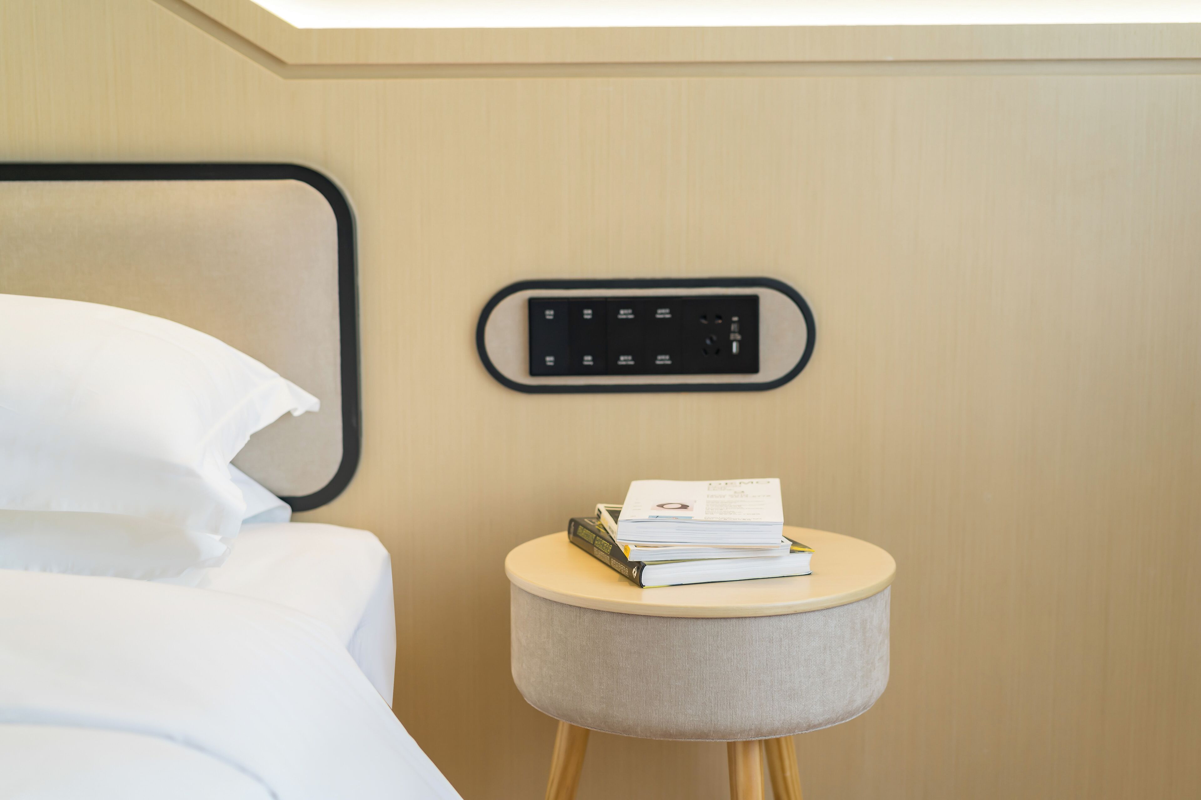 Una cama bien hecha con ropa blanca, una mesita de noche con lámpara y un panel de control en la pared.