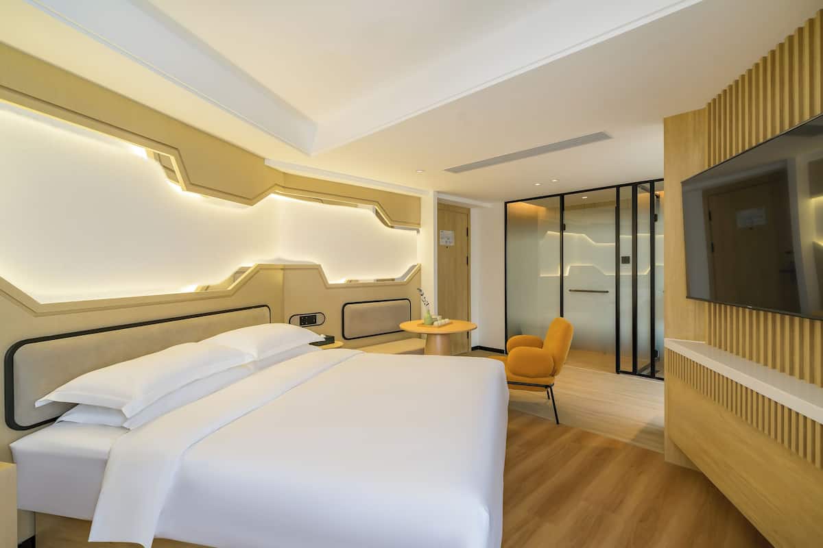 A modern hotel room with a large bed, a TV, a small table, and a chair.