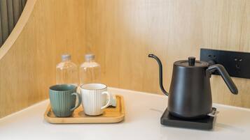 A kitchen area with a coffee maker, two mugs, and two bottles on a wooden tray.