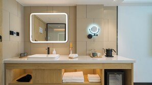 Ein modernes Badezimmer mit großem Spiegel, Waschbecken, Handtuchwärmer und kleinem Kühlschrank.