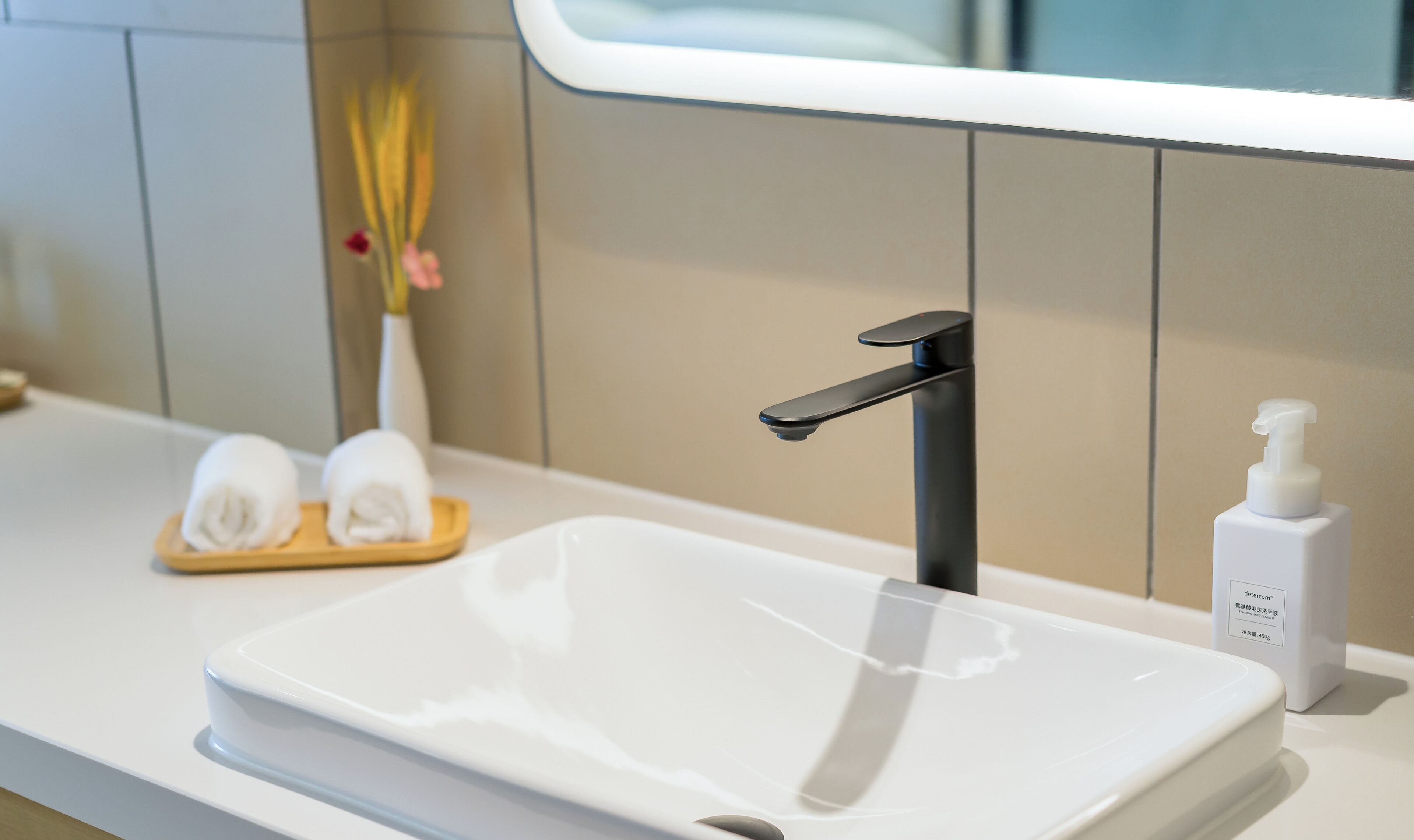 A modern bathroom with a white sink, black faucet, and a small bottle of hand soap.
